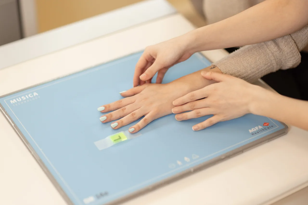 Eine Hand liegt flach auf dem Röntgendetektor, eine zweite Hand unserer Fachkraft richtet sie für die Aufnahme aus.